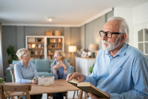 istock Senior man reading a book while two senior women chat in the background 2202675272