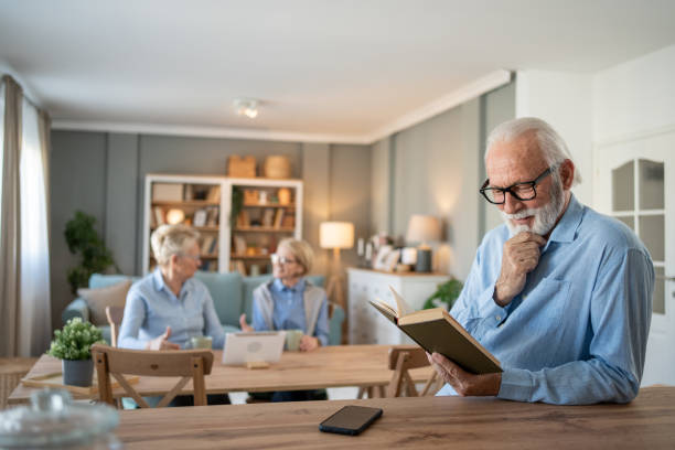 istock Senior man reading a book while two senior women chat in the background 2202675322