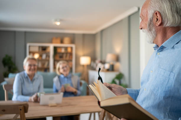 istock Senior man reading a book while two senior women chatting in the background 2202675337