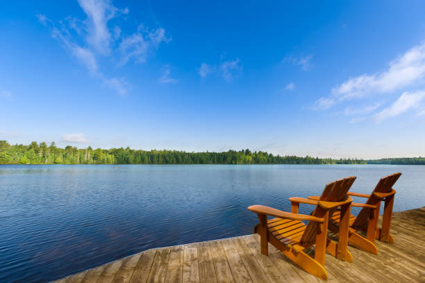 istock Adirondack chairs on a dock facing a peaceful blue lake. 2202682103