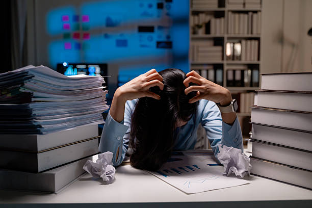 istock Stressed female professional gripping hair, working late amid scattered paperwork, experiencing workplace exhaustion and mounting pressure 2202686719