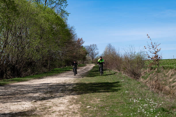 istock Two cyclists enjoy a sunny ride down a country lane, surrounded by lush greenery. 2202688622