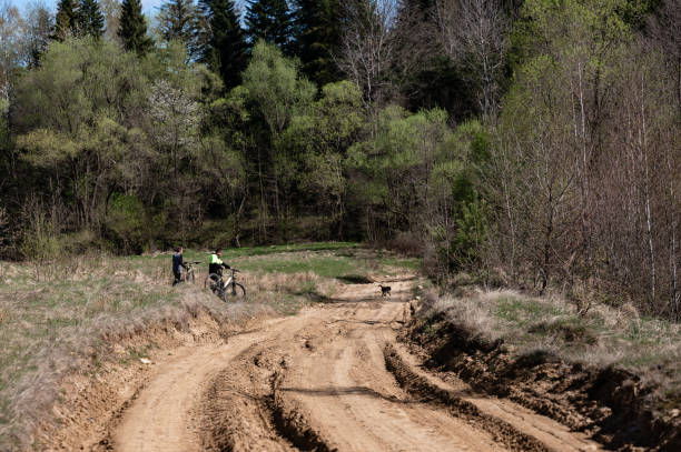 istock Two cyclists pause by a dirt road, surrounded by lush greenery and a tranquil forest. 2202688663