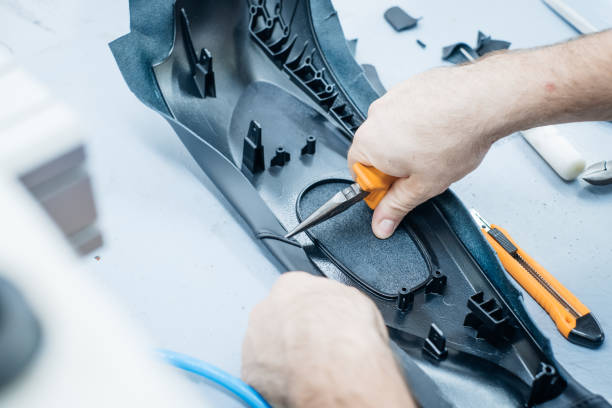 istock Crafting with precision: A worker meticulously fits trim onto a dark plastic component with specialized tools 2202688682