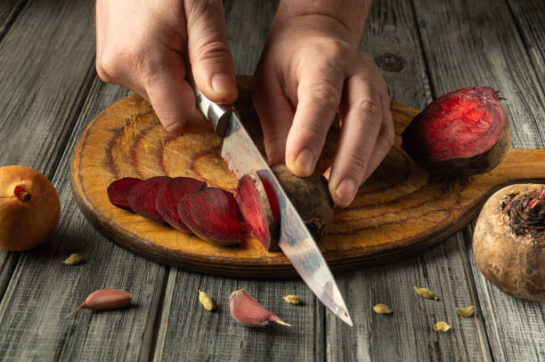 Hands expertly slice through vibrant beets, revealing their rich color, while garlic and cardamom rest nearby on a weathered wooden cutting board