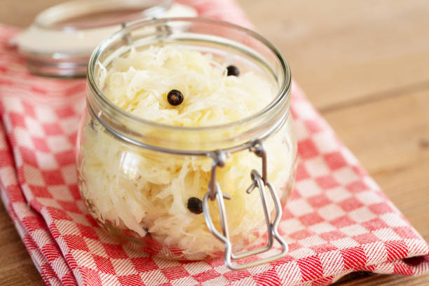 Glass jar filled with sauerkraut and juniper berries, on rustic wooden board and red queckered kitchen towel,seen from above