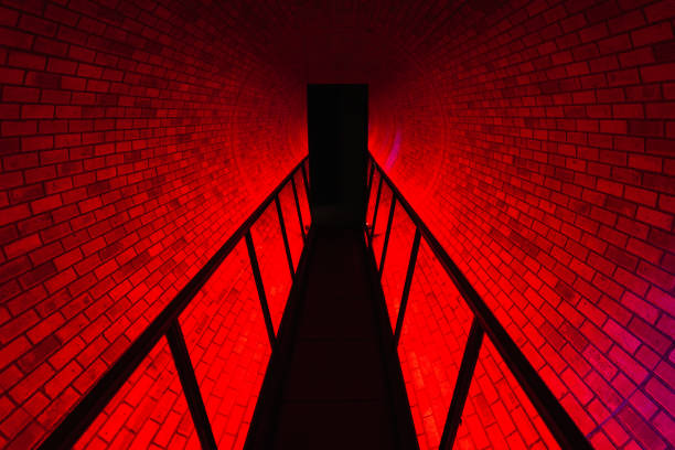 Red brick tunnel with a symmetrical corridor leading into darkness, illuminated by dramatic red light, creates an abstract geometric pattern.