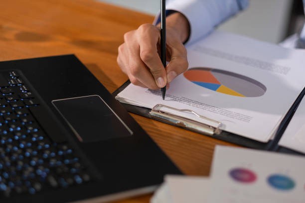 istock Businessman working at office desk analyzing financial charts and taking notes, with laptop and documents 2202711246