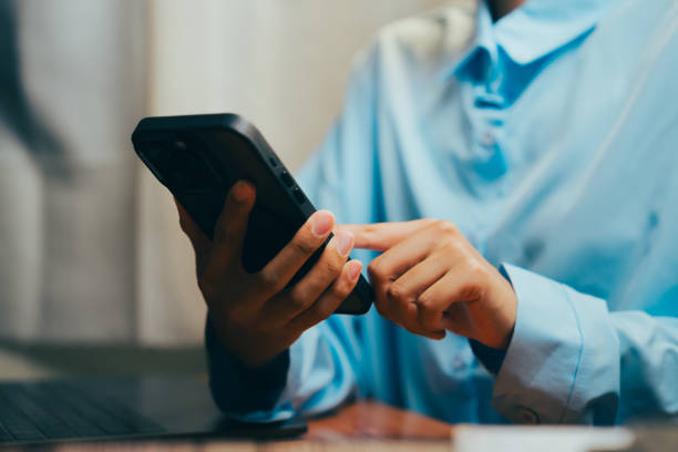 istock Person using smartphone while sitting at a table with laptop in a cozy indoor setting, Business concept. 2202713594