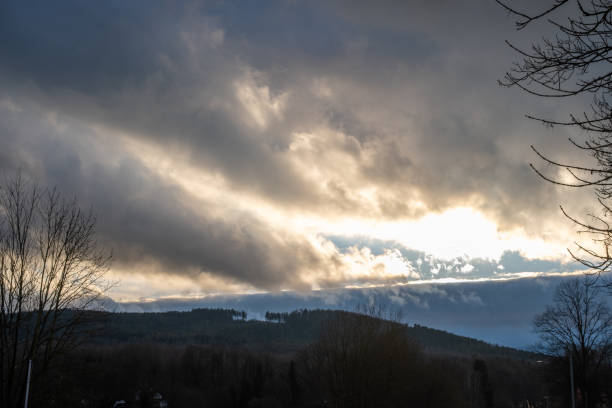 Dark clouds with sunlight breaking through over forested hills. Landscape shot capturing dramatic weather and moody atmosphere.