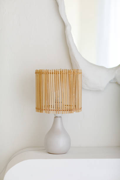 istock Scandinavian minimalistic interior design with table rattan lamp, eucalyptus branches in glass vase on shelf and mirror with textured white plaster frame on wall in light living room. Cozy home decor 2202721659