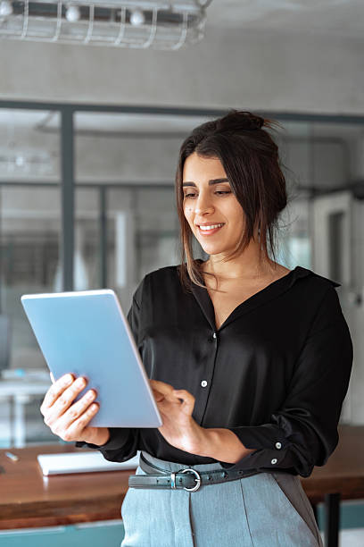istock 30s Latin Hispanic young professional business woman working on touchscreen computer. Middle eastern Indian businesswoman CEO holding digital tablet using tab application standing in office. Vertical 2202724785
