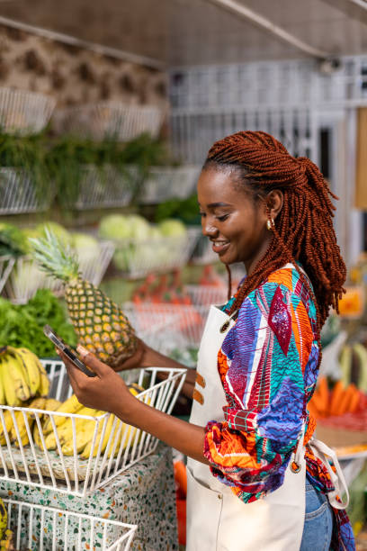 istock Successful Black female African entrepreneur holding her smartphone, chats remotely with customers and make banking transactions at her grocery shop where she sells fruits and vegetables. 2202732607
