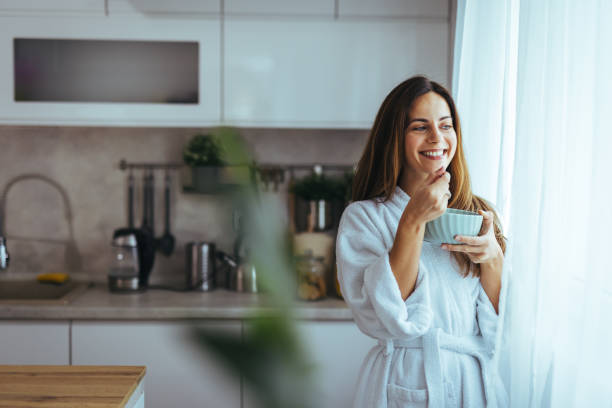 istock Smiling Woman in Bathrobe Enjoying Breakfast by Kitchen Window 2202738587