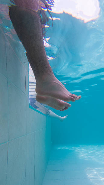 istock Individual's feet in a crystal-clear swimming pool 2202742514