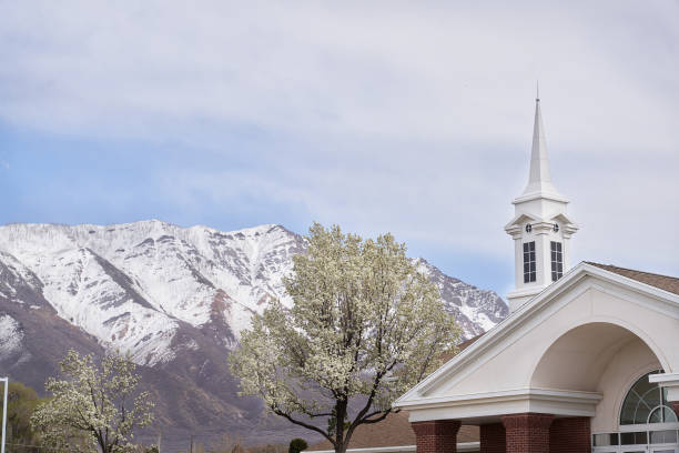 A white steepled church set against a snow covered mountains with blooming trees.