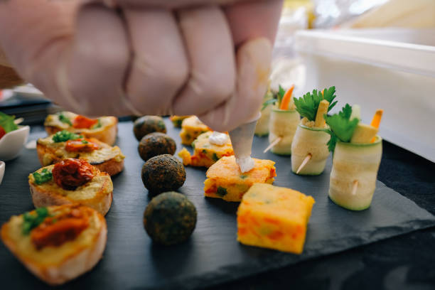 istock Catering small bites on display: Chef putting a dollop of sauce on a vegetable based snack arrangement of falafel tapas & zucchini rolls 2202749162