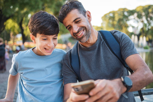 istock Father and son smiling while looking at a smartphone outdoors 2202750372