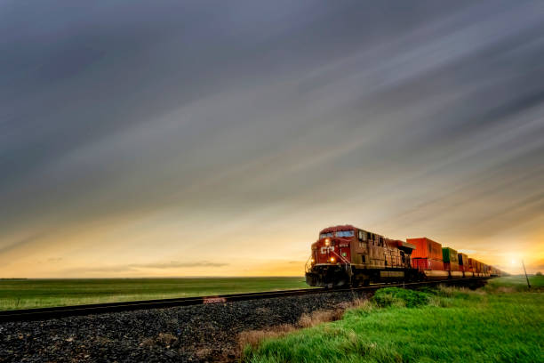 Freight train passing through countryside at sunset with dramatic sky