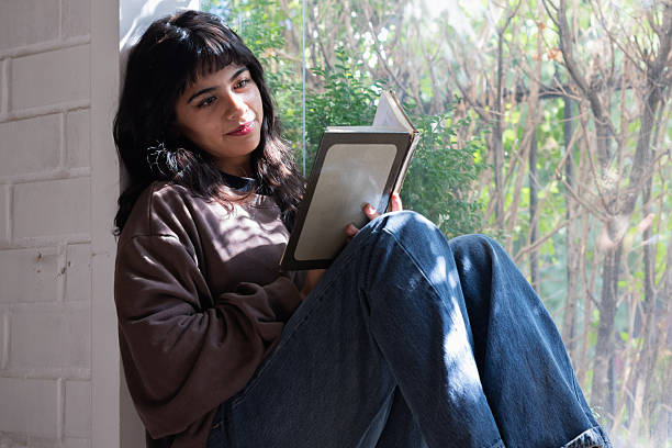istock woman student sitting by the window reading a book 2202760161