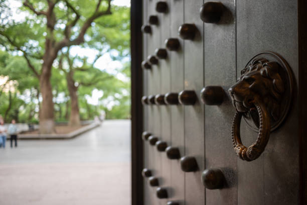 A close-up of a traditional Chinese door with a lion head knocker, set against a blurred background of lush greenery and a park.