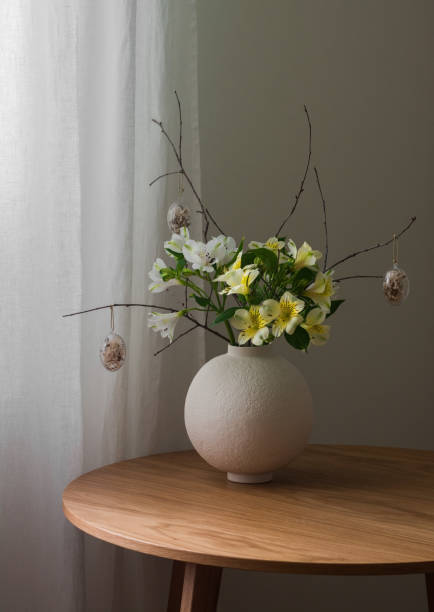 istock Easter composition with fresh flowers, branches and decorative eggs in a ceramic round vase on a wooden table 2202770000