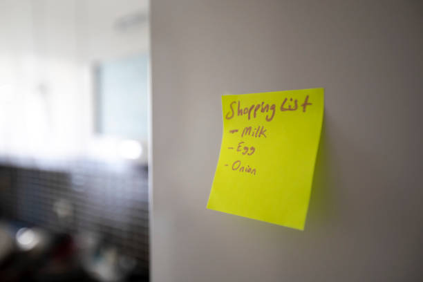 A close-up of a refrigerator with one yellow pop-up note attached. And note includes shopping list.