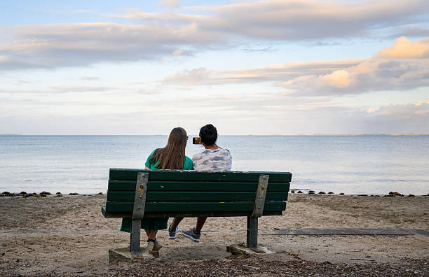 istock Two women taking selfie using a smartphone at beach. Auckland. 2202777525
