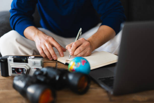 istock Tourist planning next trip writing on notebook with laptop and binoculars 2202784142