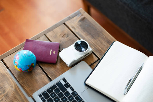 Travel blogger preparing next vacation trip using laptop, camera, passport and notepad