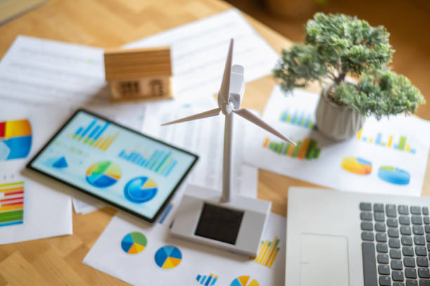 istock Miniature wind turbine and solar panel models arranged on a desk with financial charts and a digital tablet highlight an engineer assessing renewable energy investments 2202790903