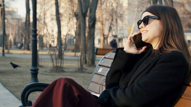 Young woman talking on smartphone while sitting on bench in park