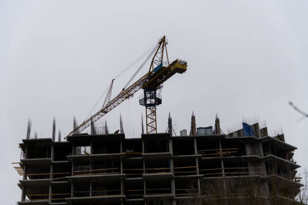 Russia, Podolsk - November 14, 2024: Construction crane is positioned at building site, actively lifting materials. Workers can be seen on-site as the grey clouds loom overhead, indicating an overcast day.