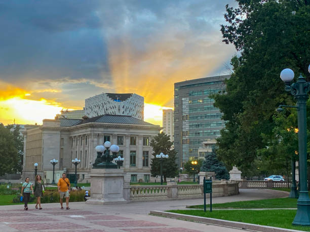 Denver, Colorado, USA - 17 July 2024: People stroll through a park at sunset, with buildings and a dramatic sky in the background in Denver Colorado.