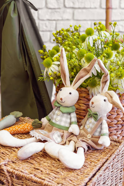 istock Decorative toy bunnies with carrots on wicker surface on flower bouquet background 2202804253