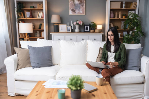 istock Concentrated millennial girl sit on couch working on laptop browsing internet at home during lazy weekend, focused young woman freelancer busy using computer surfing wireless web shopping online 2202804976