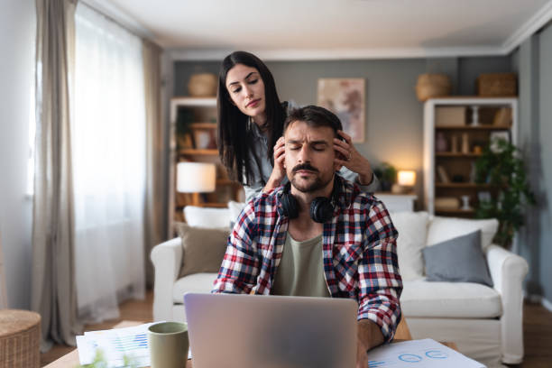 istock Young woman support her man massaging him while he work on laptop computer in home office, stressed with neck or headache pain. Love and respect. Couple simple living concept. 2202804998