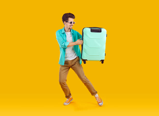 istock Happy tourist man with suitcase pointing index finger to side 2202809181