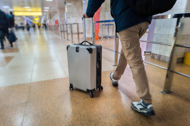 A man pushes a rolling suitcase through a brightly lit airport terminal, wearing casual clothing and a backpack, symbolizing travel and mobility.