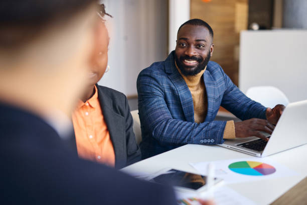 istock Smiling businessman using laptop during a meeting with colleagues in modern office 2202814306