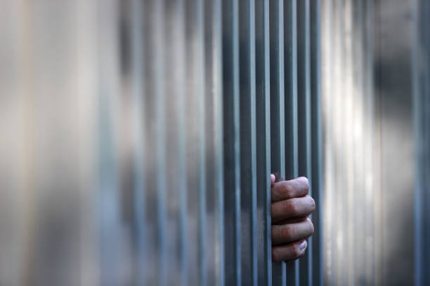 istock Hand Grasping Metal Bars in Abstract Background of a Jail Setting 2202816490