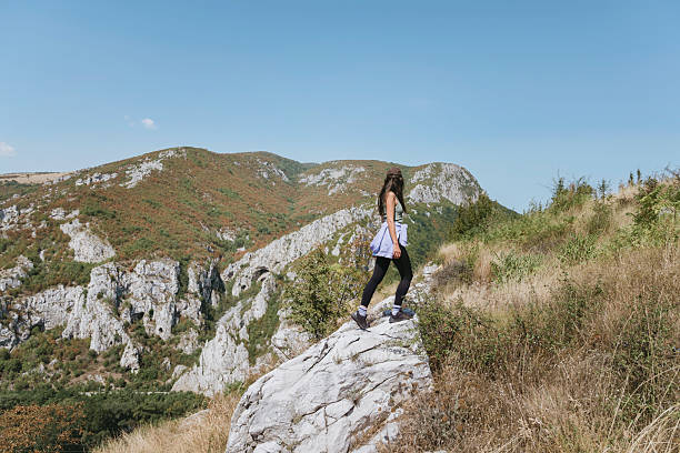 A lone hiker stands on the edge of the cliff in Caucasus, overlooking a vast valley and blue sky. High quality photo