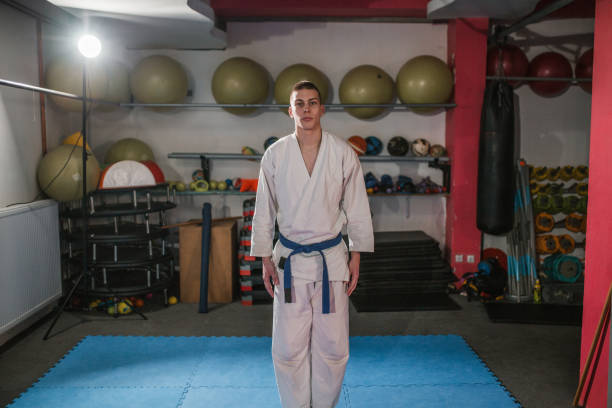 Portrait of a young aikido fighter dressed in traditional aikido clothing standing in a gym and looking directly at the camera