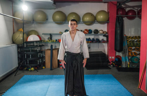 Portrait of an experienced aikido master dressed in traditional clothing standing in a gym and looking directly into the camera