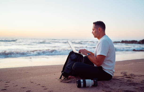 istock Photographer working on laptop at sunset on the beach 2202821891
