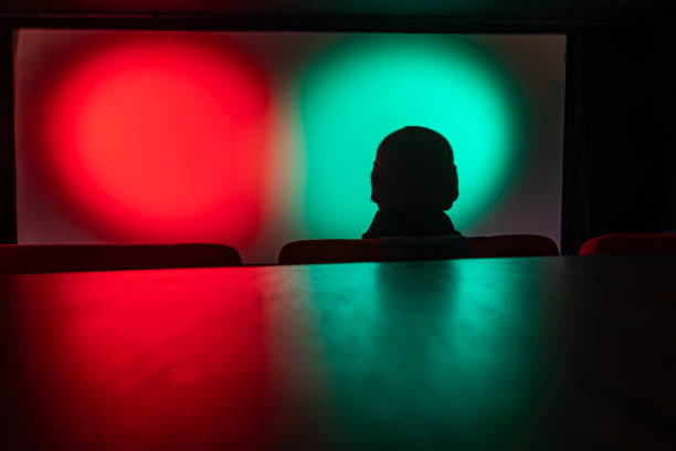 Stockholm, Sweden A man with a beanie hat sits alone in a movie theater in front of a colorful green and red screen.