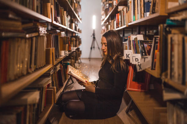 istock Carefee female student enjoys reading in the library while sitting between bookshelves 2202828439