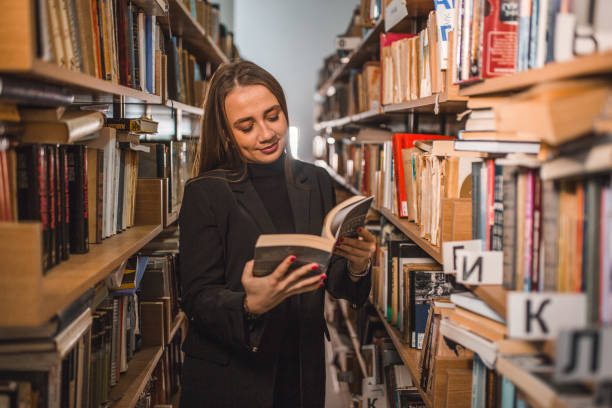 A beautiful librarian is standing between the bookshelves looking for a book she wants to read