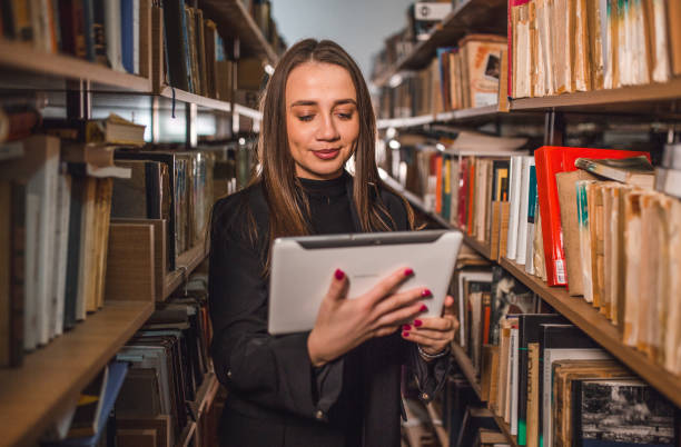 istock Lovely librarian searches books in the library using a digital tablet 2202829595