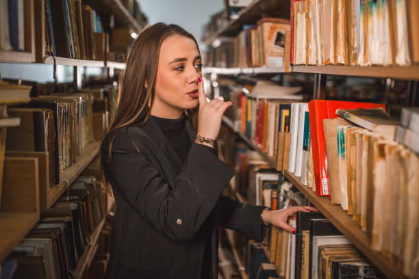 The librarian holds her finger to her lips as a sign for silence to the people in the library